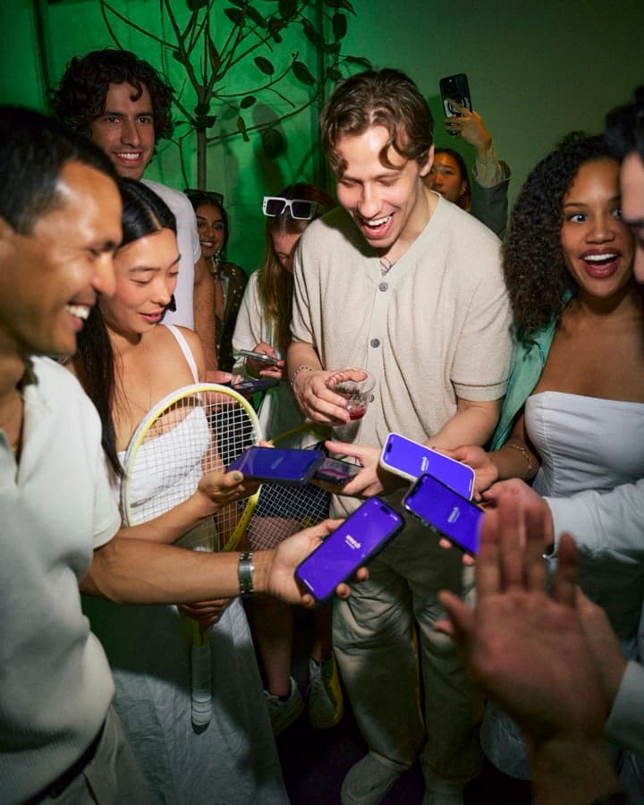 A group of guests laughing over the sponsor's app at a Mesh tennis mixer